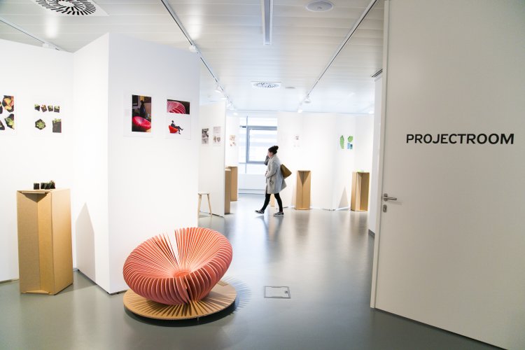 A view of the white gallery space with pictures on the walls and an interesting pink fan-shaped armchair. 


